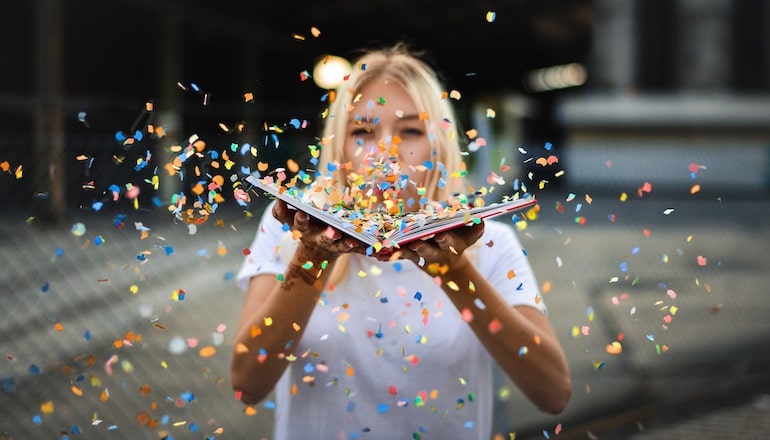 Une femme soufflant sur des confettis posés sur un livre © Paul Stachowiak / Pixabay